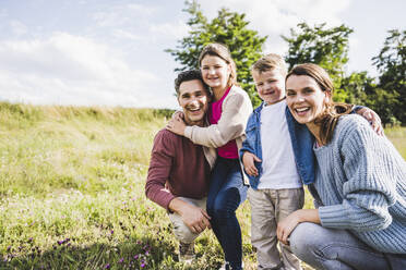 Happy parents crouching by children on meadow - UUF24240