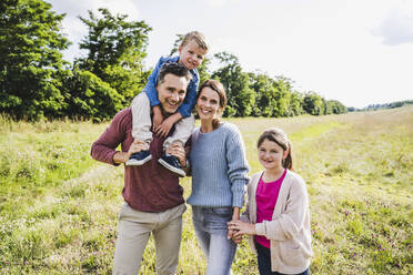 Man carrying boy on shoulders while standing with woman and daughter at meadow - UUF24242