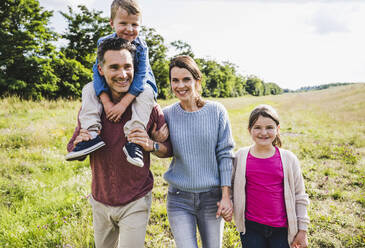 Smiling family walking at meadow on sunny day - UUF24244