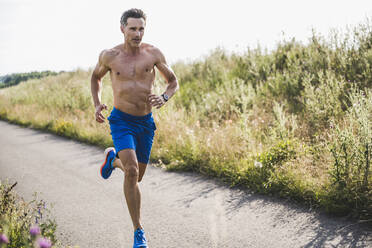 Mature shirtless sportsman running on road during sunny day - UUF24252