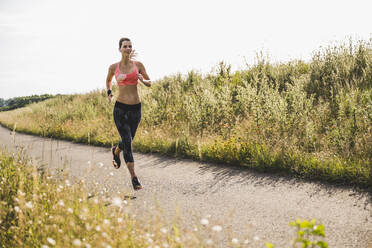 Sportswoman running on road by meadow - UUF24253