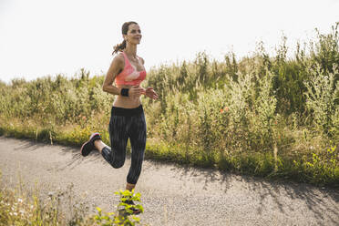 Female athlete with wireless-in ear headphones running on road - UUF24254