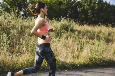 Woman with wireless in-ear headphones running by meadow - UUF24255