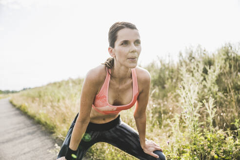 Exhausted sportswoman breathing while bending over on road - UUF24265