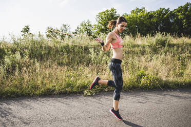 Female athlete practicing jump rope on road - UUF24267