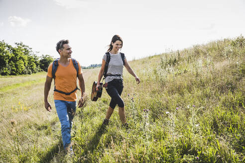 Couple with backpacks and guitar walking at meadow - UUF24278