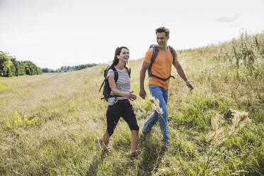 Smiling couple with backpacks hiking together on grass during sunny day - UUF24279