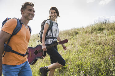 Lächelnde Frau mit Gitarre geht an einem Mann im Gras vorbei - UUF24280