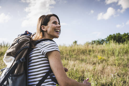 Fröhliche Frau mit Rucksack, die an einem sonnigen Tag wegschaut - UUF24281