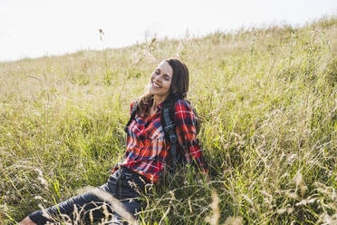 Lächelnde Frau, die auf einer Wiese sitzt und sich entspannt - UUF24289