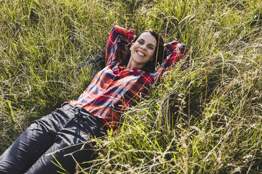 Smiling woman with hands behind head lying on grass - UUF24290