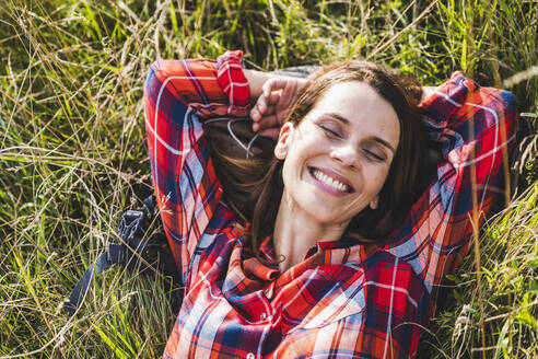 Cheerful woman with eyes closed lying on grass - UUF24292