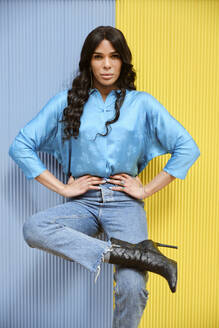 Fashionable female transgender with hand on hip leaning on corrugated wall - AODF00575