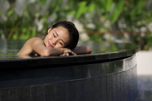 Woman with eyes closed resting at poolside - EAF00031