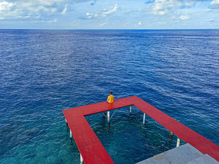 Mann auf rotem Steg auf der Insel Thulusdhoo im Kaafu-Atoll, Malediven - KNTF06349