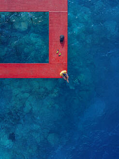 Man sitting on red pier over sea at Thulusdhoo Island in Kaafu Atoll, Maldives - KNTF06350