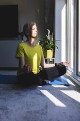 Woman meditating in lotus position at home - WPEF05091