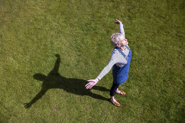 Mature woman with arms outstretched on grass during sunny day - WPEF05113