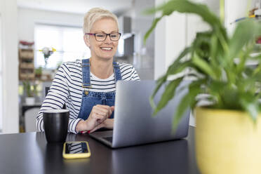 Smiling businesswoman looking at laptop on desk in home office - WPEF05120