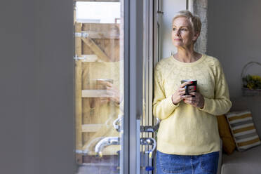 Frau hält Tasse, während sie zu Hause vor der Tür steht - WPEF05134