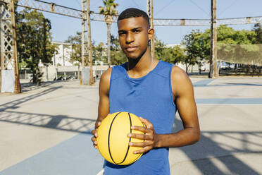 Junger Mann hält Basketball auf einem Sportplatz - XLGF02119