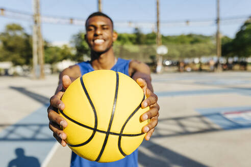 Lächelnder Mann hält gelben Basketball auf dem Sportplatz - XLGF02122