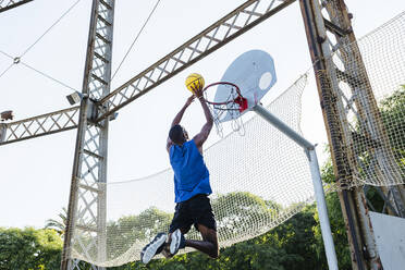 Young man dunking basketball while playing at sports court - XLGF02127