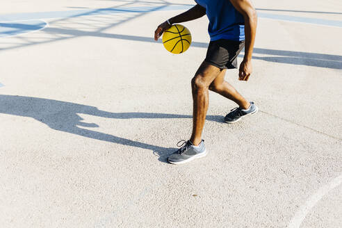 Junger Mann dribbelt Basketball auf einem Sportplatz an einem sonnigen Tag - XLGF02128