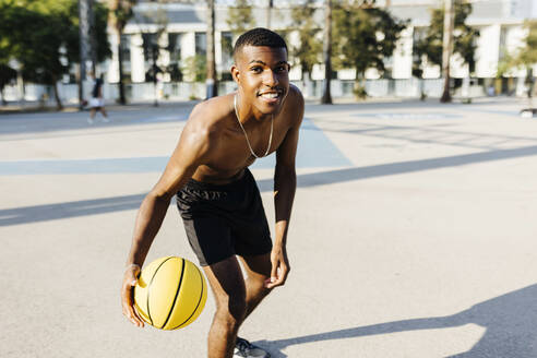 Shirtless young man practicing basketball at sports court - XLGF02140
