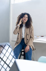 Geschäftsfrau, die im Büro sitzend mit einem Mobiltelefon telefoniert - GIOF13090