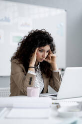 Angespannte Geschäftsfrau mit Kopf in den Händen sitzt im Büro - GIOF13107