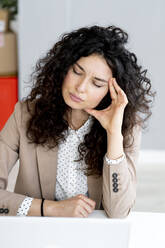 Businesswoman with eyes closed sitting at desk in office - GIOF13109