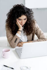 Nachdenkliche Geschäftsfrau mit Blick auf den Laptop auf dem Schreibtisch - GIOF13110