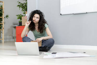 Thoughtful businesswoman sitting with laptop on floor - GIOF13114