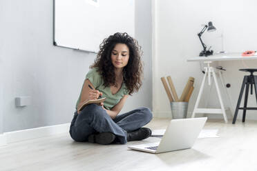 Businesswoman writing on paper while sitting with cross-legged on floor in office - GIOF13117