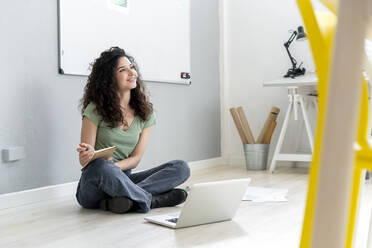 Businesswoman contemplating while sitting with laptop on floor in office - GIOF13118