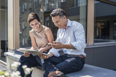 Smiling male and female colleagues using digital tablet - UUF24311