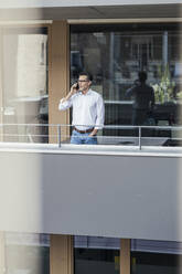 Geschäftsmann, der auf dem Balkon eines Büros steht und mit seinem Handy telefoniert - UUF24349