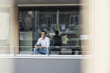 Geschäftsmann mit digitalem Tablet auf dem Balkon eines Büros sitzend - UUF24352