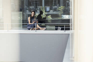 Geschäftsfrau mit digitalem Tablet auf dem Balkon eines Büros sitzend - UUF24355