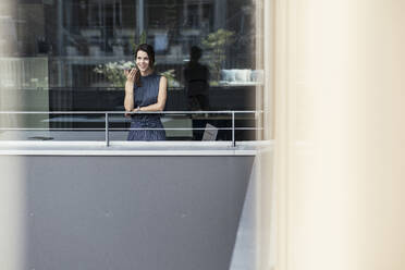 Businesswoman talking on mobile phone at office balcony - UUF24356