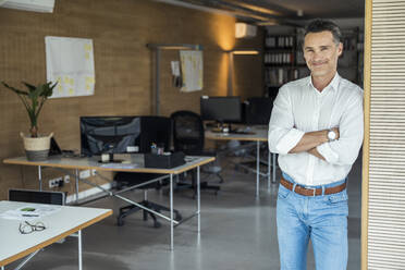 Smiling businessman with arms crossed standing in office - UUF24368