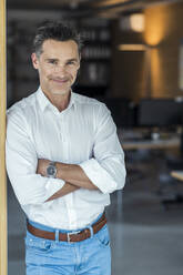 Smiling businessman with arms crossed standing at office - UUF24370