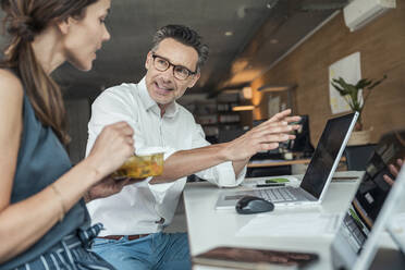 Geschäftsmann zeigt auf Laptop, während er einem Kollegen im Büro etwas erklärt - UUF24375