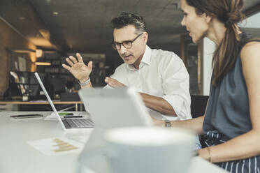 Male professional explaining over laptop to female colleague in office - UUF24376