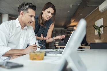 Business professionals discussing over laptop in office - UUF24378