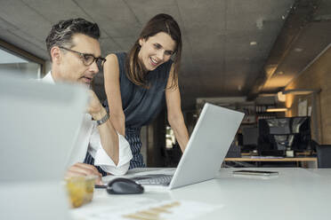 Male and female professionals using laptop while working in office - UUF24379