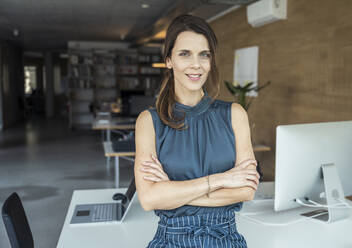 Confident businesswoman with arms crossed standing in office - UUF24380