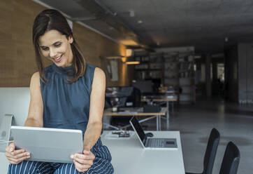 Female professional using digital tablet while sitting on desk - UUF24382