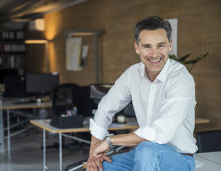 Smiling businessman sitting at workplace - UUF24391